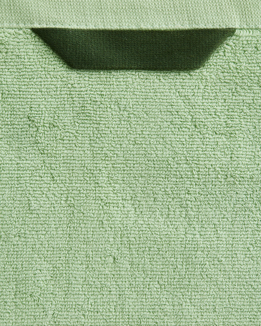 A close-up of the Bed Threads Apple 100% Cotton Terry Bath Sheet Bundle in light green, featuring a dark green fabric loop at the top edge, set against a matching green background.