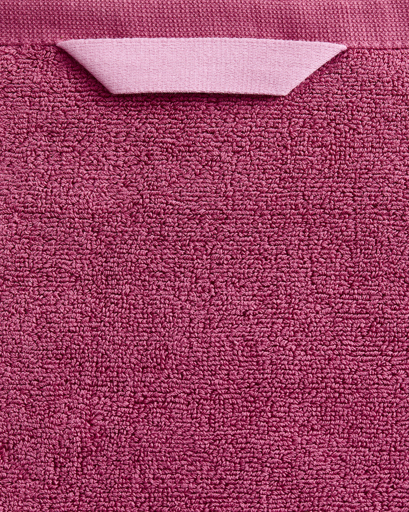 A close-up of the Bed Threads Berry 100% Cotton Terry Bath Sheet, featuring a plush pink texture and a handy folded fabric loop—ideal for those seeking quick-drying comfort.