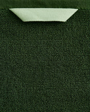 A close-up of the Bed Threads Moss 100% Cotton Terry Bath Sheet Bundle shows its rich dark green texture, with a neatly folded light green corner at the top that reveals the material’s underside. - view