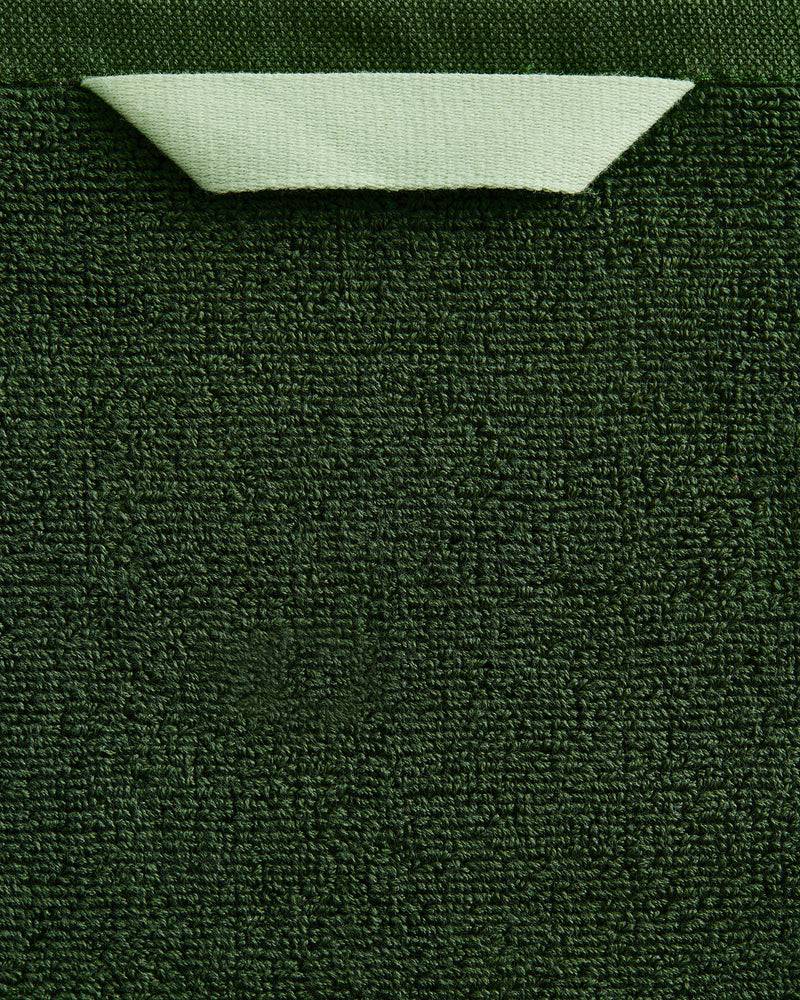 A close-up of the Bed Threads Moss 100% Cotton Terry Bath Sheet Bundle shows its rich dark green texture, with a neatly folded light green corner at the top that reveals the material’s underside.