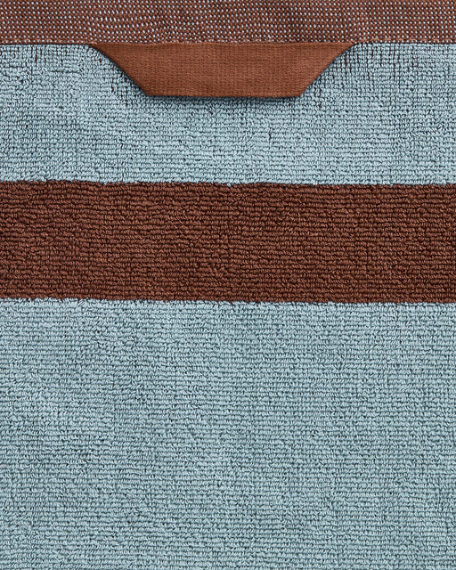 Close-up of the Bed Threads Cacao & Lagoon Two-Toned 100% Cotton Terry Bath Sheet Bundle, featuring plush light blue textured fabric, a horizontal brown stripe, and a brown loop at the top edge.