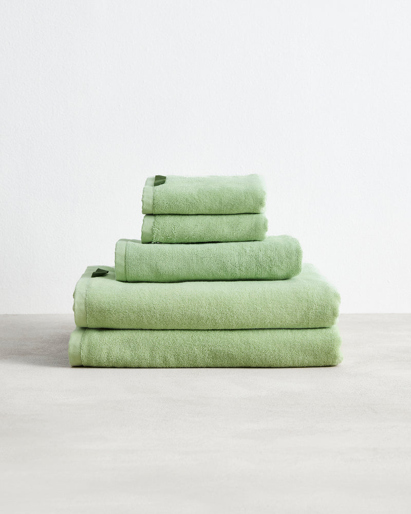 The Bed Threads Apple 100% Cotton Terry Bath Sheet Bundle features four highly absorbent, light green towels in various sizes, neatly stacked on a light surface against a plain white background.