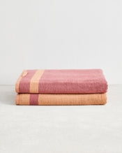 Two folded Terracotta & Pink Clay Two-Toned 100% Cotton Terry Bath Sheets by Bed Threads are stacked on a light grey surface against a white wall. - view