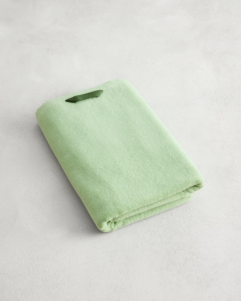 A neatly folded Apple 100% Cotton Terry Bath Towel by Bed Threads rests on a light, textured surface, highlighting its plush 650GSM softness.