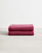 Two Berry 100% Cotton Terry Bath Towels by Bed Threads, neatly folded and stacked, shown against a plain white background. Set of two in a rich dark pink shade on a light-colored surface. - view