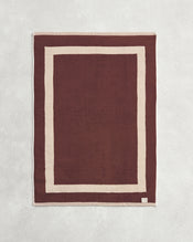 Flat cotton terry bath mat on a grey background in a cacao colour with a creme border. - view