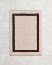 Flat cotton terry bath mat on a grey background in an oatmeal colour with a charcoal border. - view