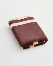 A folded cotton terry bath towel on a grey background, in a cacao colourway with a creme border.  - view