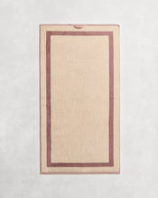 Flat cotton terry towel on a grey background in a creme colour with a lavender border. - view