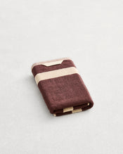 A folded cotton terry hand towel on a grey background, in a cacao colourway with a creme border.  - view