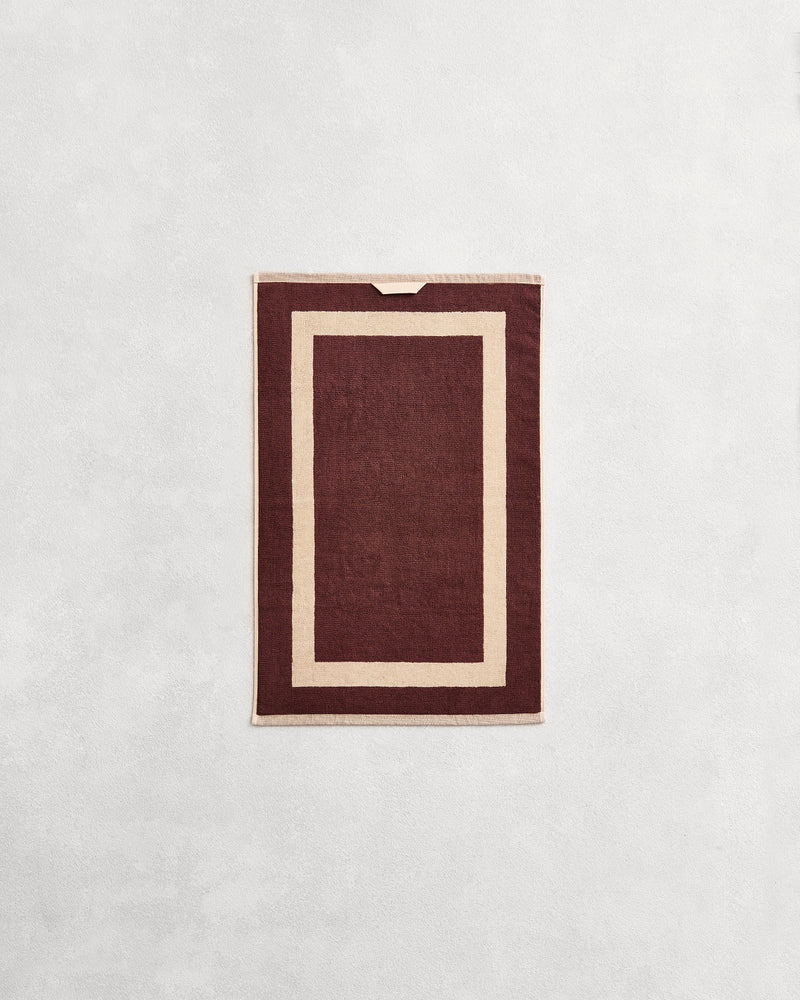 Flat cotton terry hand towel on a grey background in a cacao colour with a creme border.