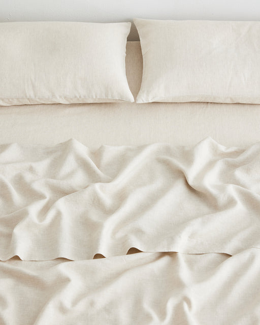 A neatly made bed with two pillows and an Oatmeal & White Stripe 100% French Flax Linen Fitted Sheet by Bed Threads, viewed from above. The minimalist bedding is crafted for comfort and features temperature-regulating linen.
