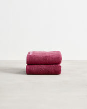 Two folded dark pink Berry 100% Cotton Terry Hand Towels by Bed Threads, from a set of two, stacked on a light surface with a plain white background. - view