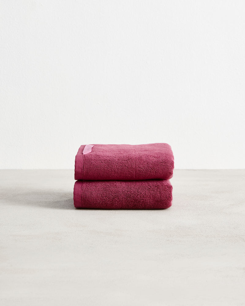 Two folded dark pink Berry 100% Cotton Terry Hand Towels by Bed Threads, from a set of two, stacked on a light surface with a plain white background.