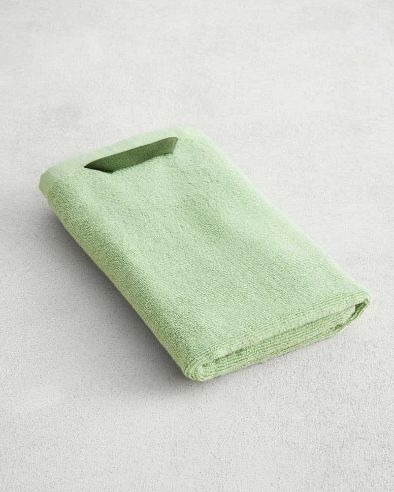 The Apple 100% Cotton Terry Hand Towel by Bed Threads, in light green, is neatly folded on a light gray textured surface, highlighting its plush 650GSM fabric for superior comfort.