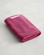 The Berry 100% Cotton Terry Hand Towel by Bed Threads, crafted from plush 650GSM maroon terry and featuring a light pink hanging loop, is displayed on a light gray surface. - view