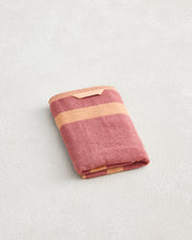 A folded Bed Threads Terracotta & Pink Clay Two-Toned 100% Cotton Terry Hand Towel with horizontal stripes rests on a light textured surface. - view