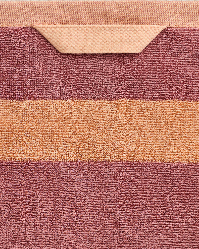 A close-up of the Bed Threads Terracotta & Pink Clay Two-Toned 100% Cotton Terry Hand Towel, showing a peach stripe and matching loop, set against muted mauve terry fabric.