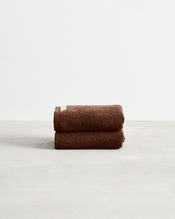 Two neatly folded Bed Threads Espresso 100% Cotton Terry Hand Towels (Set of Two) are stacked on a light surface with a white background, highlighting their soft and highly absorbent texture. - view