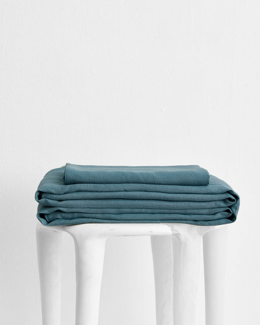 The Lagoon 100% French Flax Linen Sheet Set by Bed Threads, neatly folded atop a sculptural white stool against a plain background, exemplifies stylish bedding with exceptional temperature regulation.
