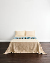 A neatly made bed with a cream quilt cover in Lagoon & Creme and matching pillowcases in Creme, set against a plain white wall and dark wood flooring. - view