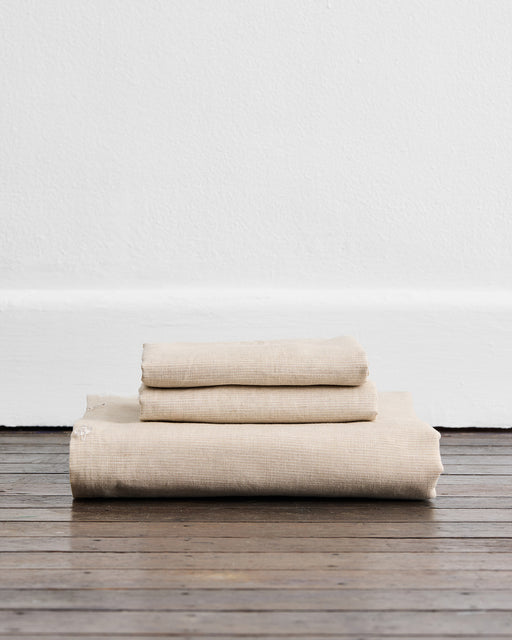The Oatmeal & White Stripe 100% French Flax Linen Duvet Cover Set by Bed Threads—three neatly folded sheets stacked, ready to pair with your luxurious duvet covers or matching pillowcases for a refined touch.