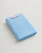 The Bed Threads Sky 100% Cotton Terry Hand Towel, light blue with a plush 650GSM texture and a small pink tag, is neatly folded on a light textured surface. - view