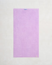 The Bed Threads Violet 100% Cotton Terry Bath Towel is a neatly rectangular, light purple towel with a blue loop on the top edge and a beige tag at the bottom right—ideal for those seeking absorbent, stylish bath linens. - view