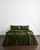 A neatly made bed features the Olive 100% French Flax Linen Duvet Cover and two matching pillows by Bed Threads, set against a white wall on wooden flooring, creating an inviting space with temperature-regulating bedding.
