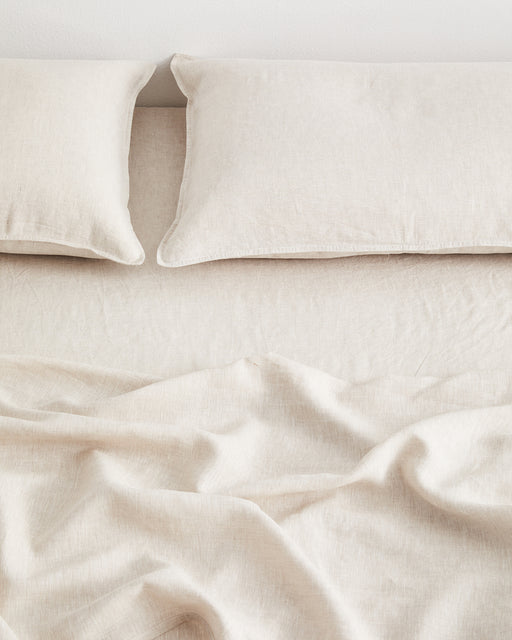 A neatly made bed features the Bed Threads Oatmeal 100% French Flax Linen Fitted Sheet and two matching pillows—one slightly askew—beneath a loosely draped blanket with gentle folds.