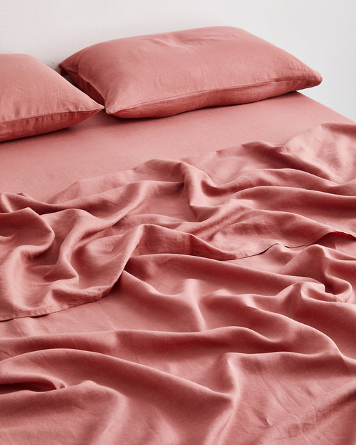 The Bed Threads Pink Clay 100% French Flax Linen Flat Sheet, paired with two pillows, is loosely draped over the bed for a relaxed, cozy look. Its naturally wrinkled texture enhances the inviting vibe.