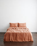 A bed featuring the Hazelnut 100% French Flax Linen Duvet Cover and two matching pillows by Bed Threads stands against a plain white wall on a dark wooden floor.
