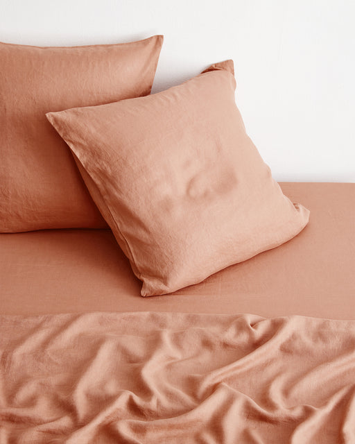 A neatly made bed features two Bed Threads Hazelnut 100% French Flax Linen European Pillowcases—one upright, one angled—against a white wall, with softly rumpled sheets in the foreground.